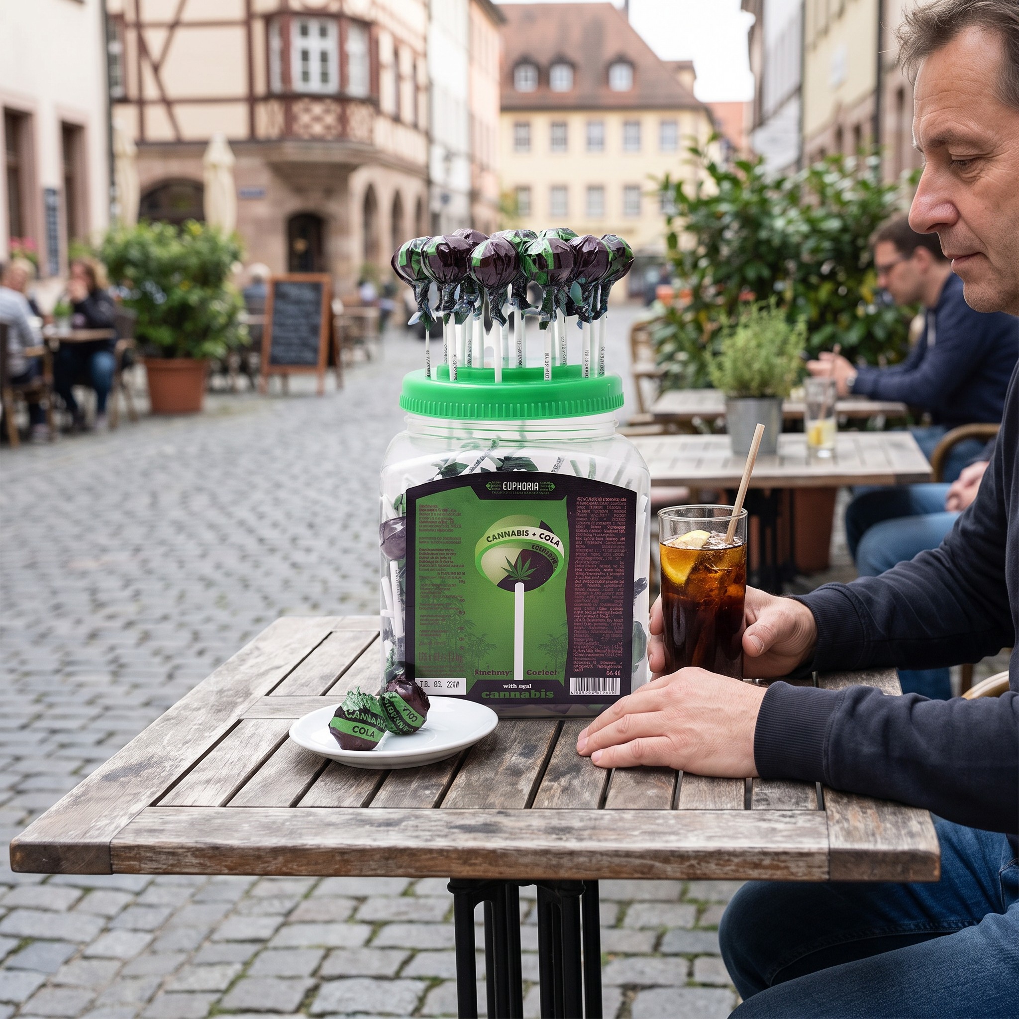 Euphoria Lollipops Cannabis Cola – Cola-Lollis mit Cola-Glas auf einem Café-Terrassentisch